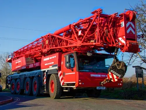 A red Sparrow Crane Hire mobile crane parked on a road, with its boom stowed