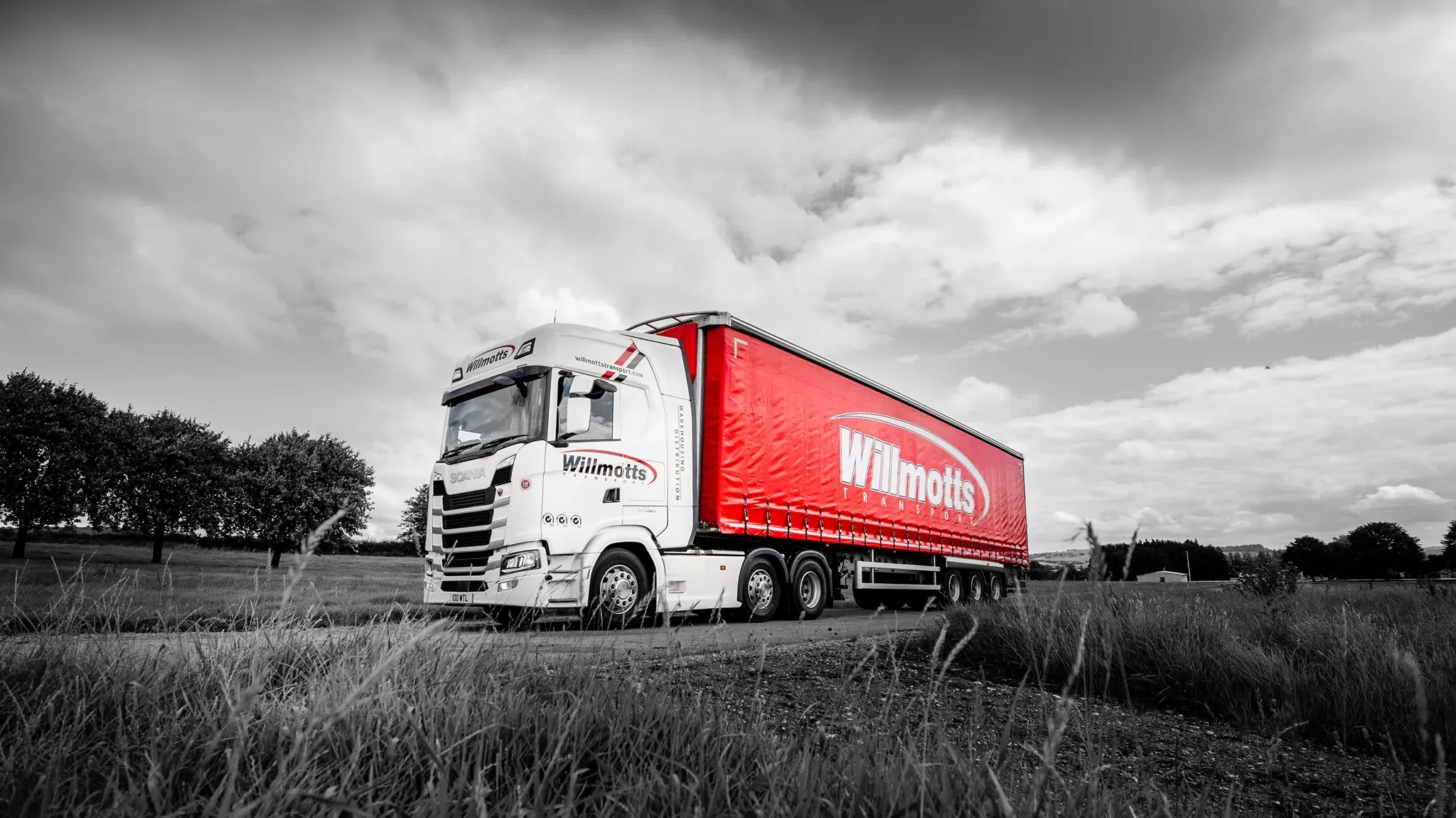 A Willmotts Transport lorry, with a white cab and a red curtain-sided trailer, on a rural road